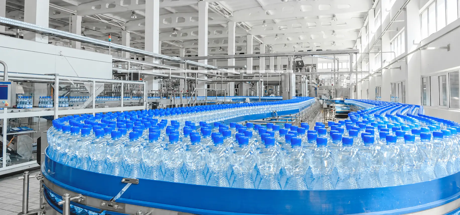 High-speed PET water bottling line with blue-capped bottles on a curved conveyor